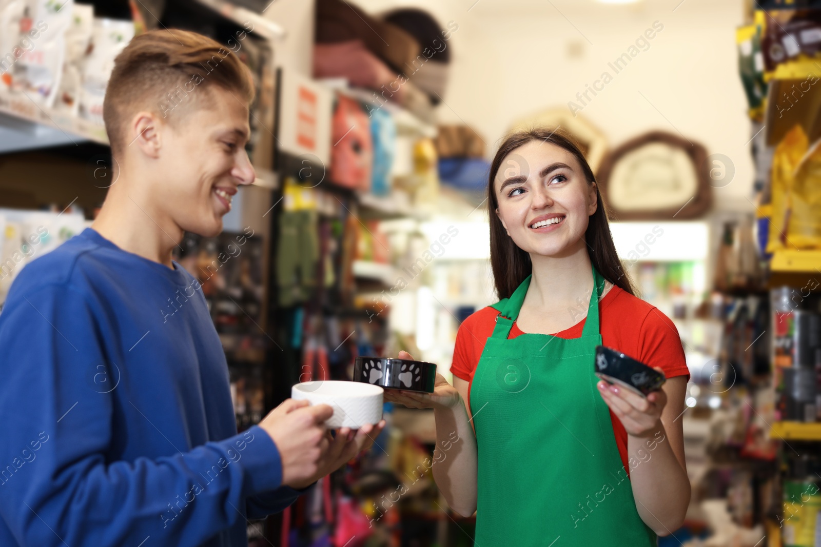 Photo of Pet shop worker helping young man choosing feeding bowl indoors