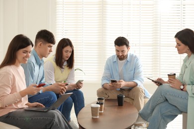 Photo of Internet addiction. Group of friends with gadgets and coffee at table indoors