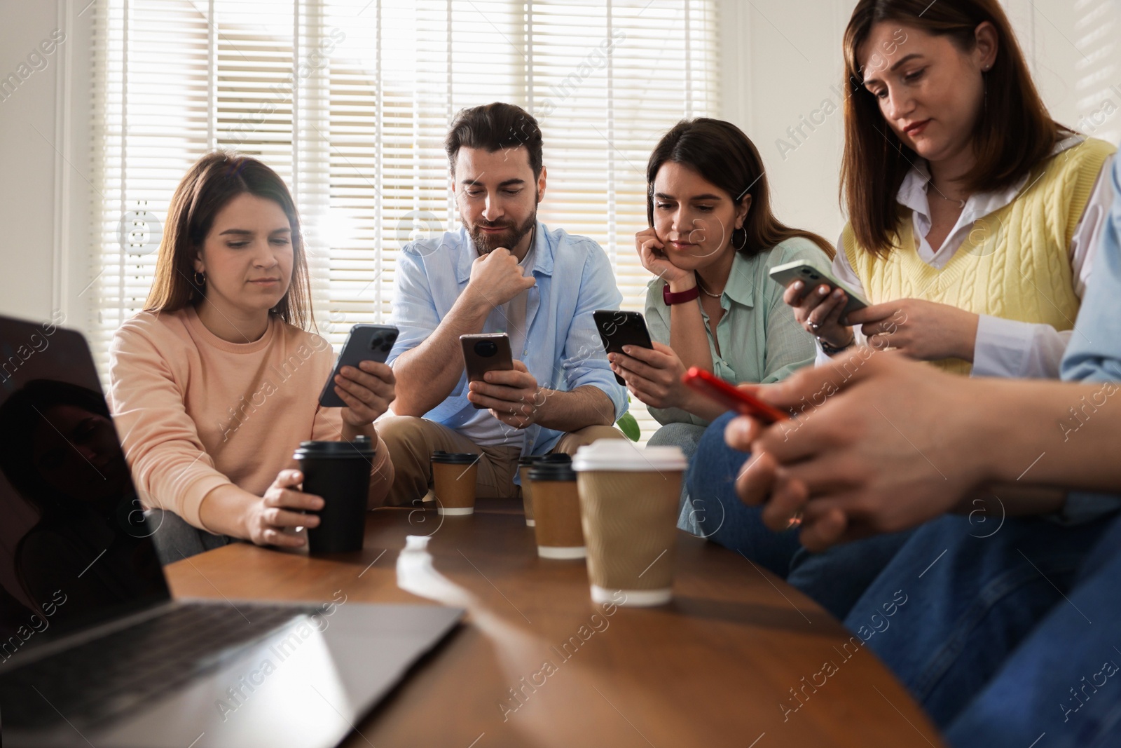 Photo of Internet addiction. Group of friends with gadgets and coffee at table indoors