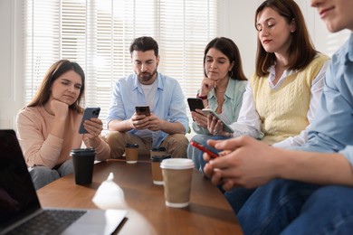 Photo of Internet addiction. Group of friends with gadgets and coffee at table indoors