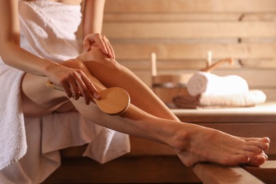 Photo of Woman massaging her leg with brush at sauna, closeup