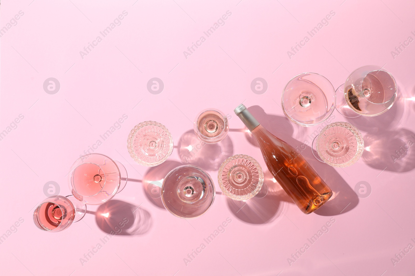 Photo of Delicious rose wine in glasses and bottle on pink background, flat lay. Space for text