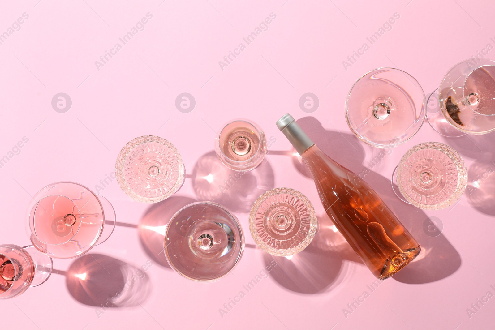 Photo of Delicious rose wine in glasses and bottle on pink background, flat lay. Space for text