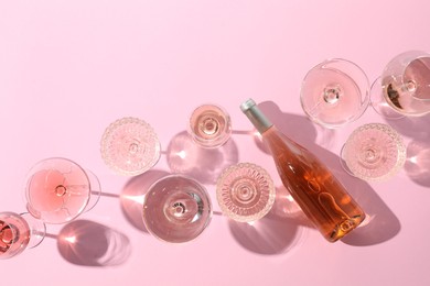 Photo of Delicious rose wine in glasses and bottle on pink background, flat lay. Space for text