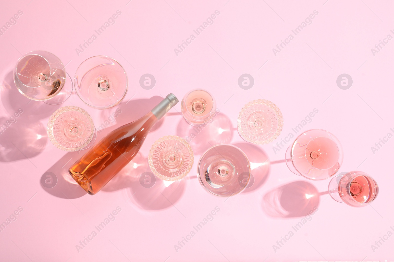 Photo of Delicious rose wine in glasses and bottle on pink background, flat lay. Space for text