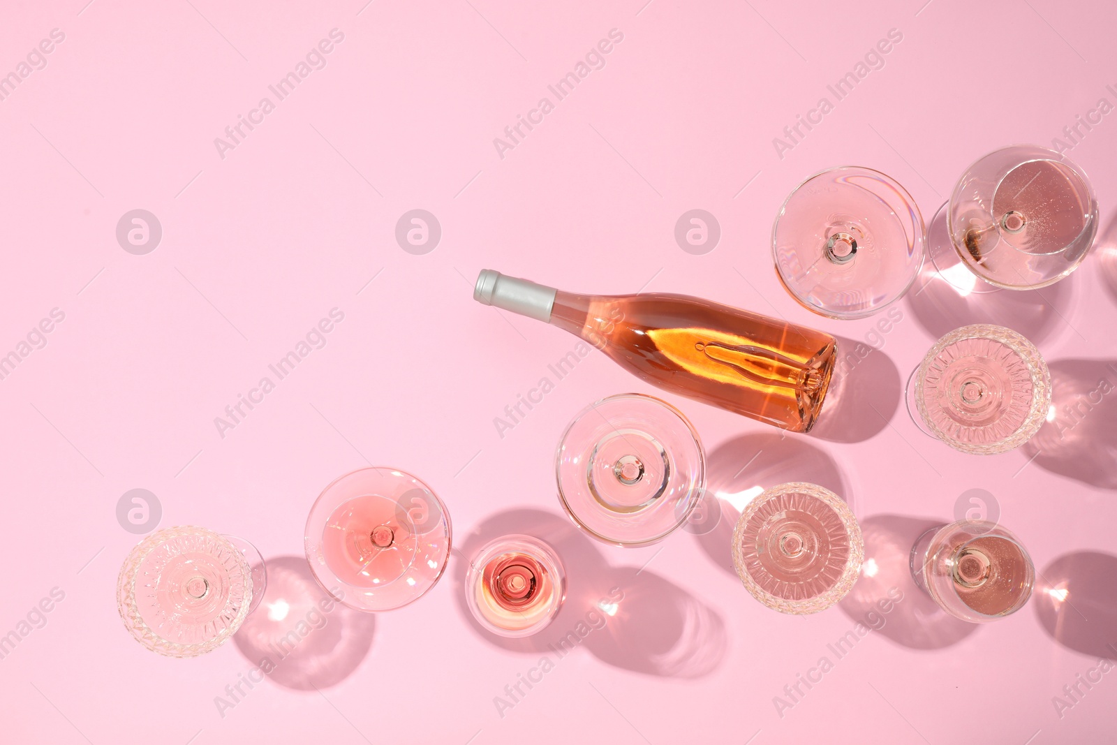 Photo of Delicious rose wine in glasses and bottle on pink background, flat lay. Space for text