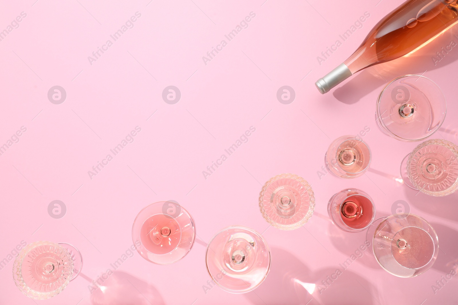 Photo of Delicious rose wine in glasses and bottle on pink background, flat lay. Space for text