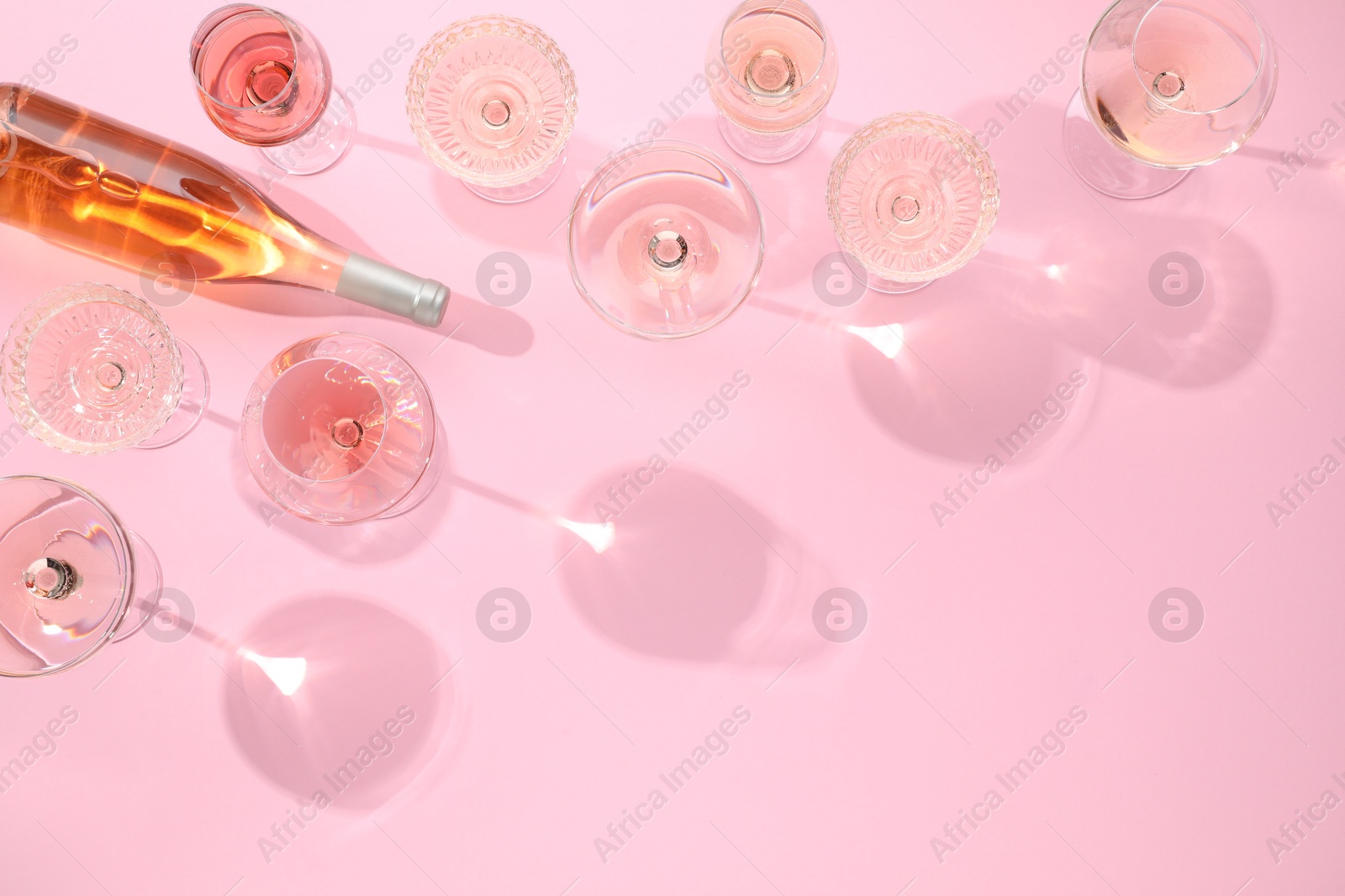 Photo of Delicious rose wine in glasses and bottle on pink background, flat lay. Space for text