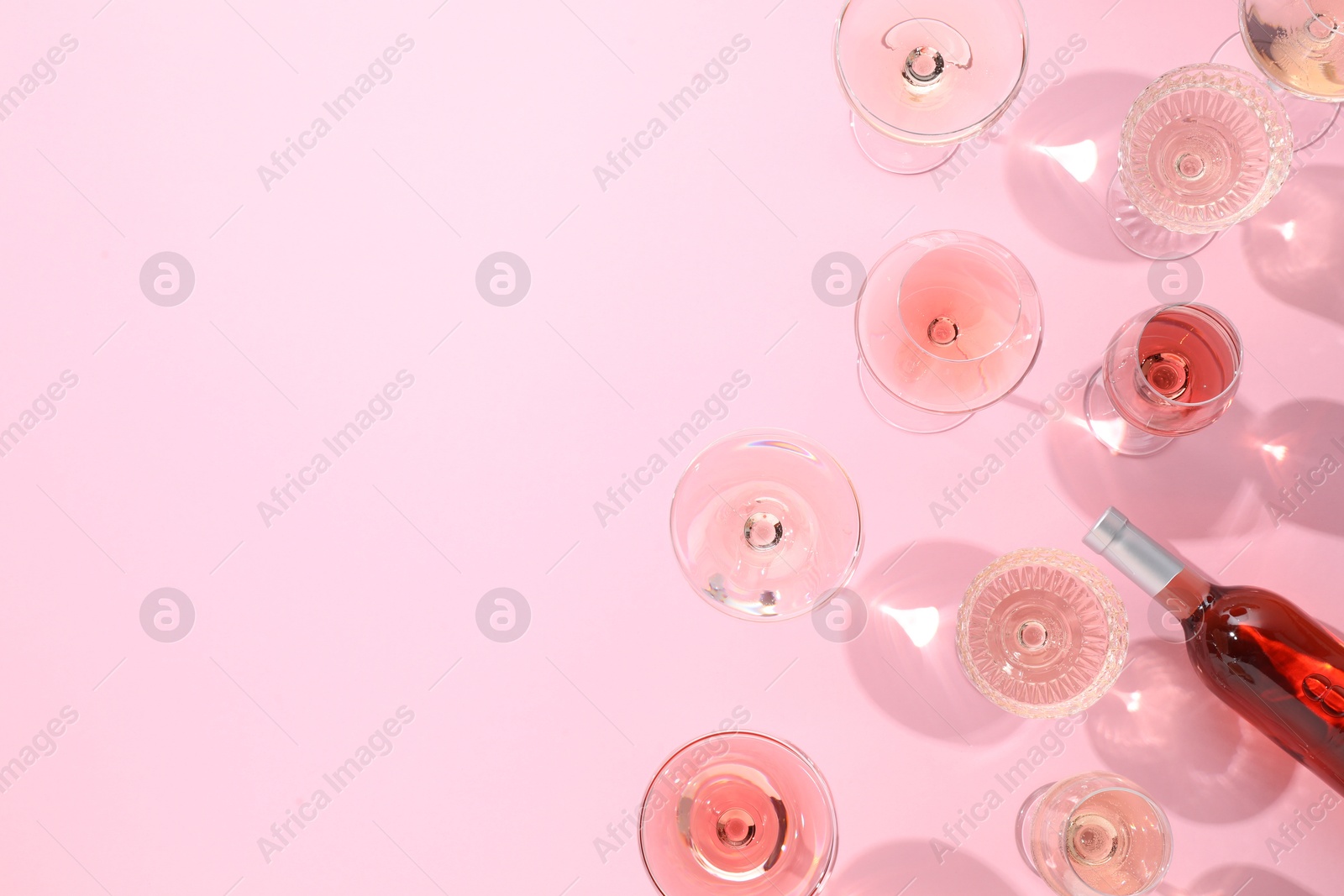 Photo of Delicious rose wine in glasses and bottle on pink background, flat lay. Space for text