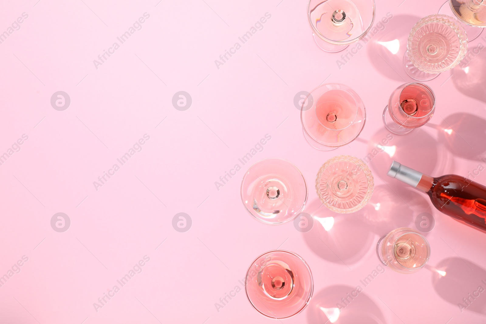 Photo of Delicious rose wine in glasses and bottle on pink background, flat lay. Space for text