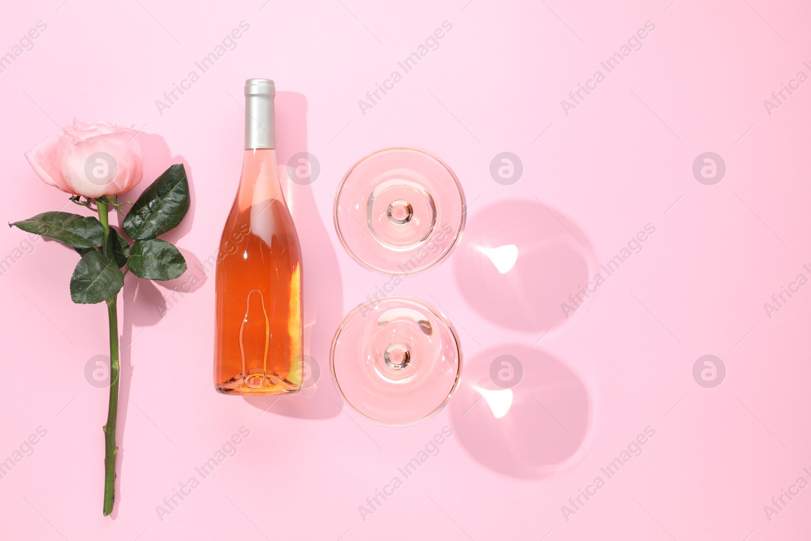 Photo of Delicious rose wine in glasses and bottle with flower on pink background, flat lay