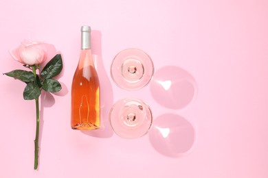 Delicious rose wine in glasses and bottle with flower on pink background, flat lay