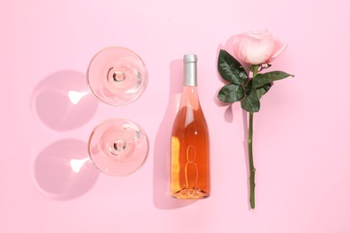 Delicious rose wine in glasses and bottle with flower on pink background, flat lay