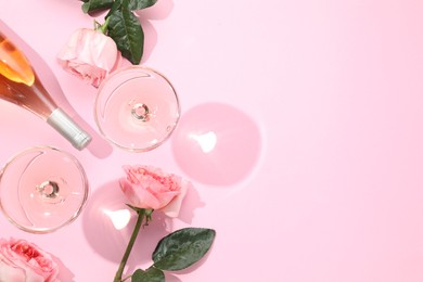 Delicious rose wine in glasses and bottle with flowers on pink background, flat lay. Space for text