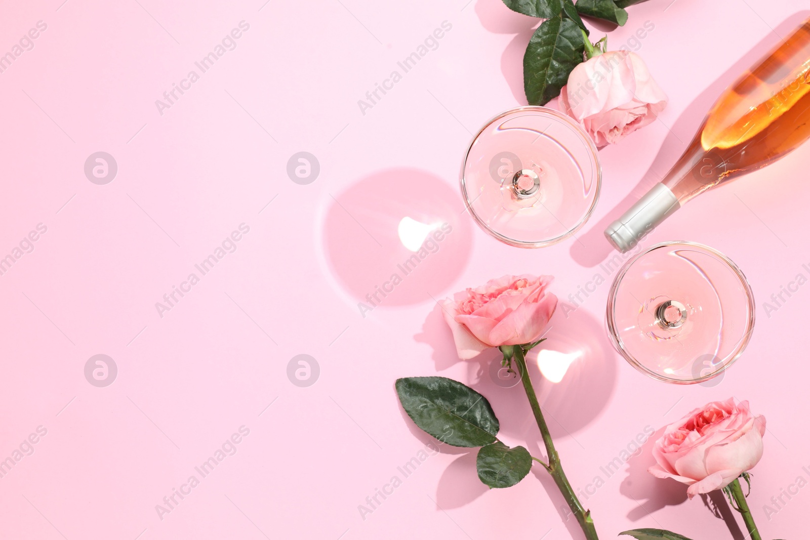 Photo of Delicious rose wine in glasses and bottle with flowers on pink background, flat lay. Space for text