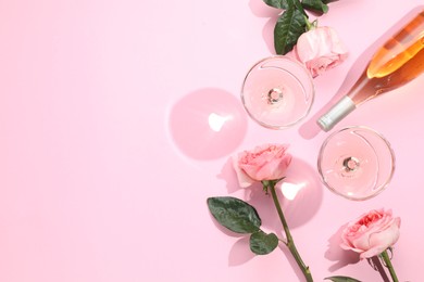 Delicious rose wine in glasses and bottle with flowers on pink background, flat lay. Space for text