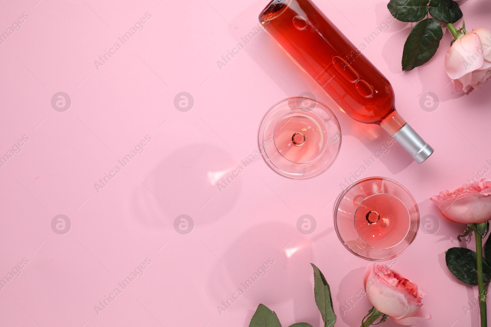 Photo of Delicious rose wine in glasses and bottle with flowers on pink background, flat lay. Space for text