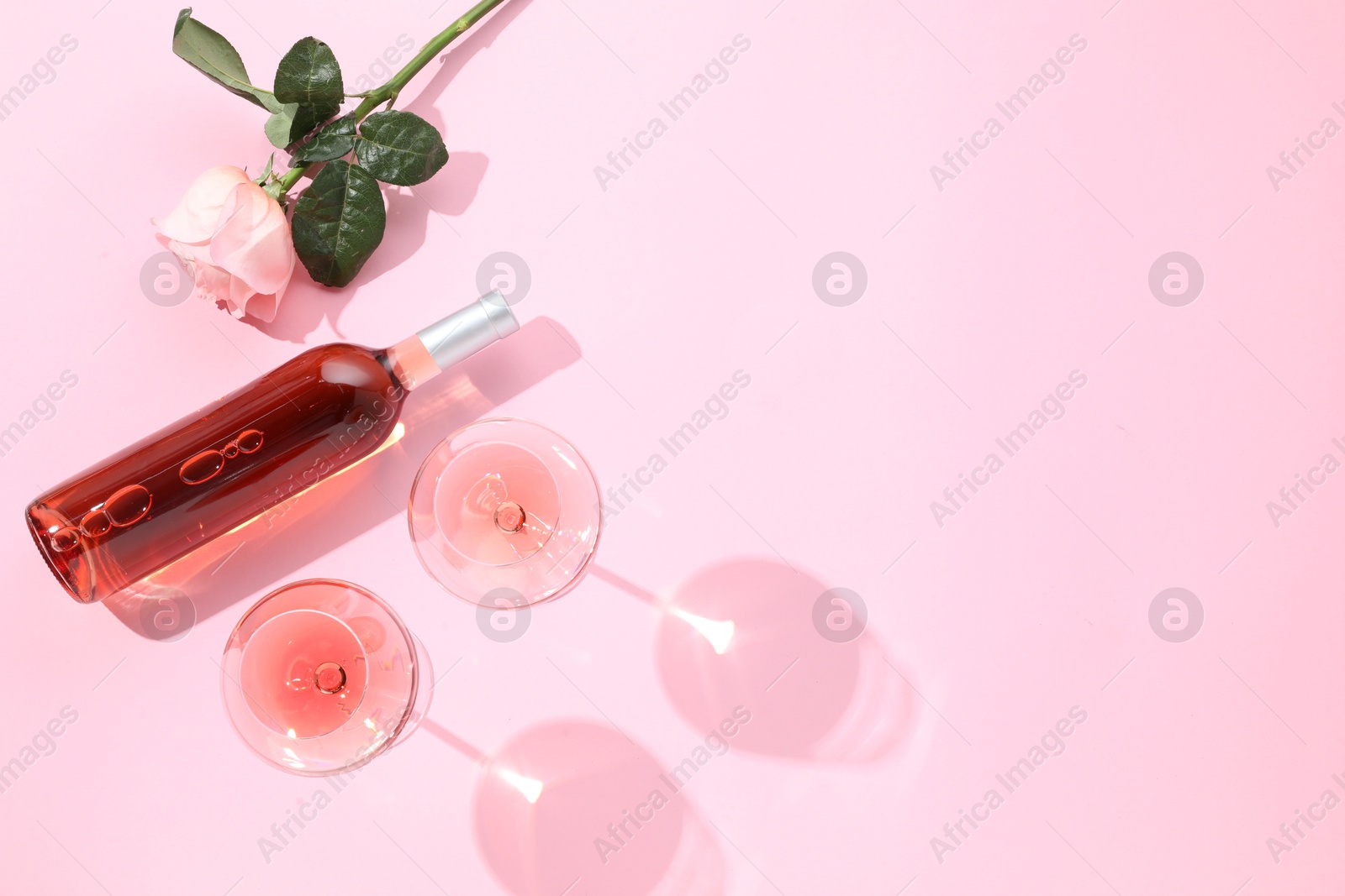 Photo of Delicious rose wine in glasses and bottle with flower on pink background, flat lay. Space for text