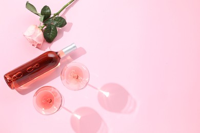 Delicious rose wine in glasses and bottle with flower on pink background, flat lay. Space for text