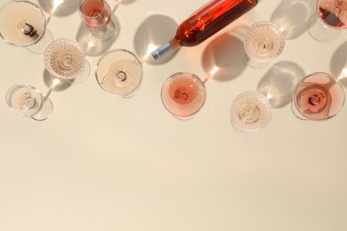 Photo of Delicious rose wine in glasses and bottle on beige background, flat lay. Space for text