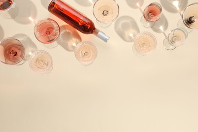 Delicious rose wine in glasses and bottle on beige background, flat lay. Space for text