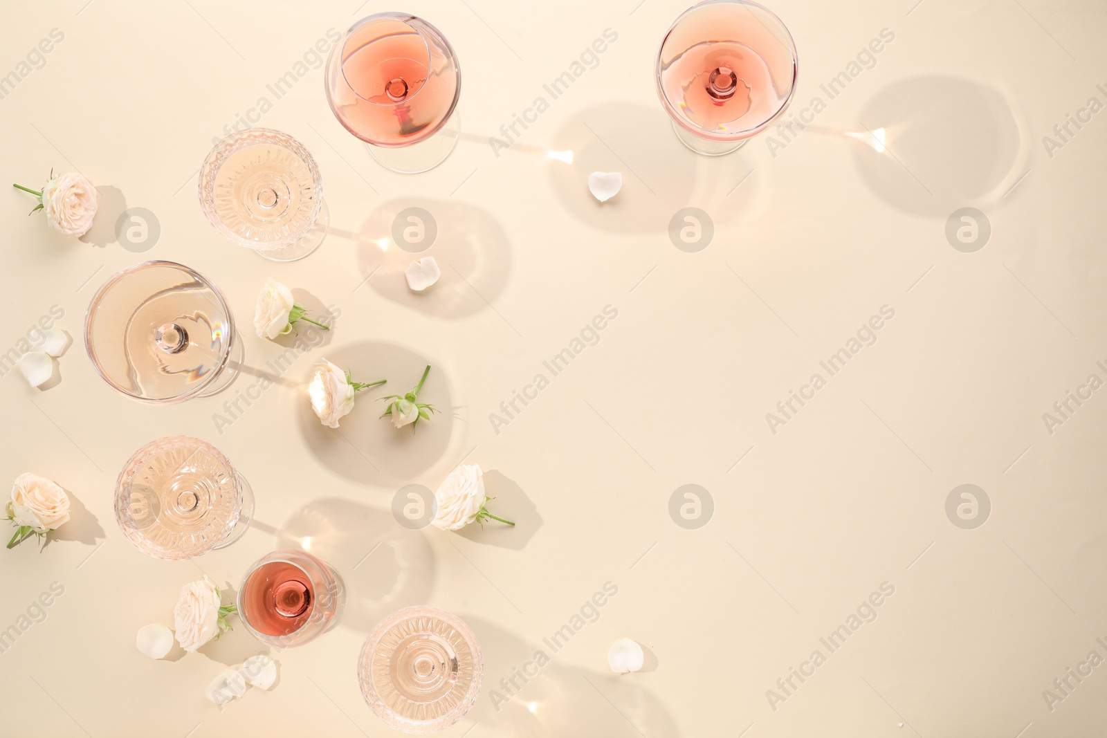 Photo of Delicious rose wine in glasses and flowers on beige background, flat lay. Space for text