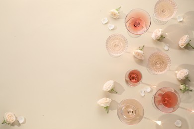 Photo of Delicious rose wine in glasses and flowers on beige background, flat lay. Space for text