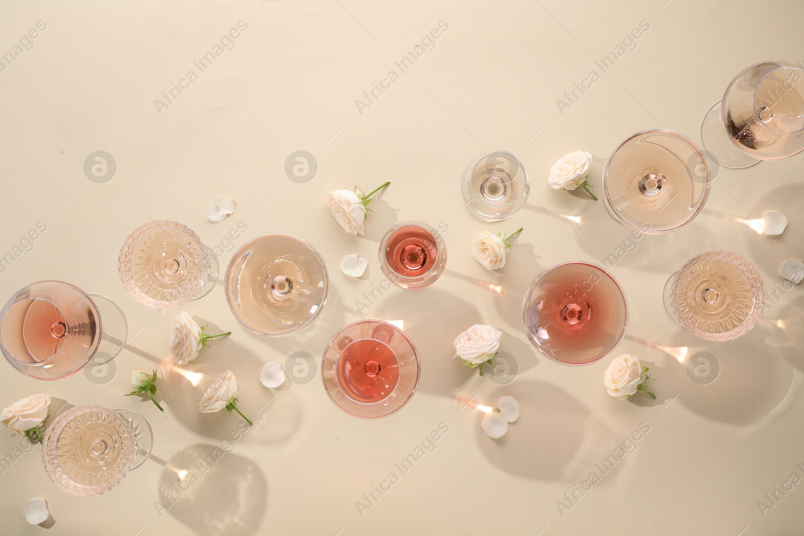 Photo of Delicious rose wine in glasses and flowers on beige background, flat lay. Space for text