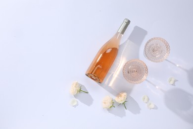 Delicious rose wine in glasses and bottle with flowers on white background, flat lay. Space for text