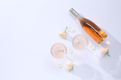 Photo of Delicious rose wine in glasses and bottle with flowers on white background, flat lay