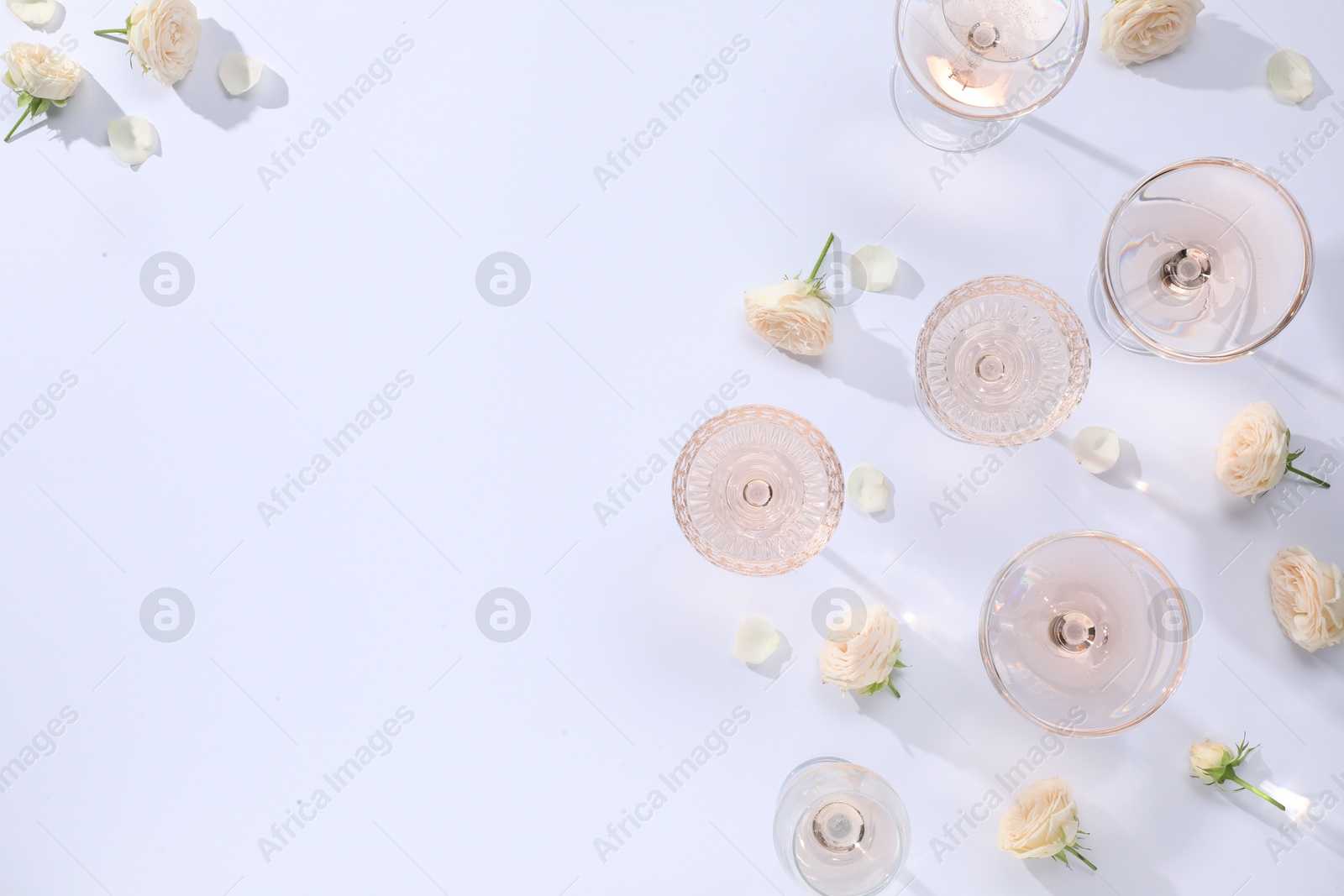 Photo of Delicious rose wine in glasses and flowers on white background, flat lay. Space for text