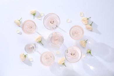 Delicious rose wine in glasses and flowers on white background, flat lay