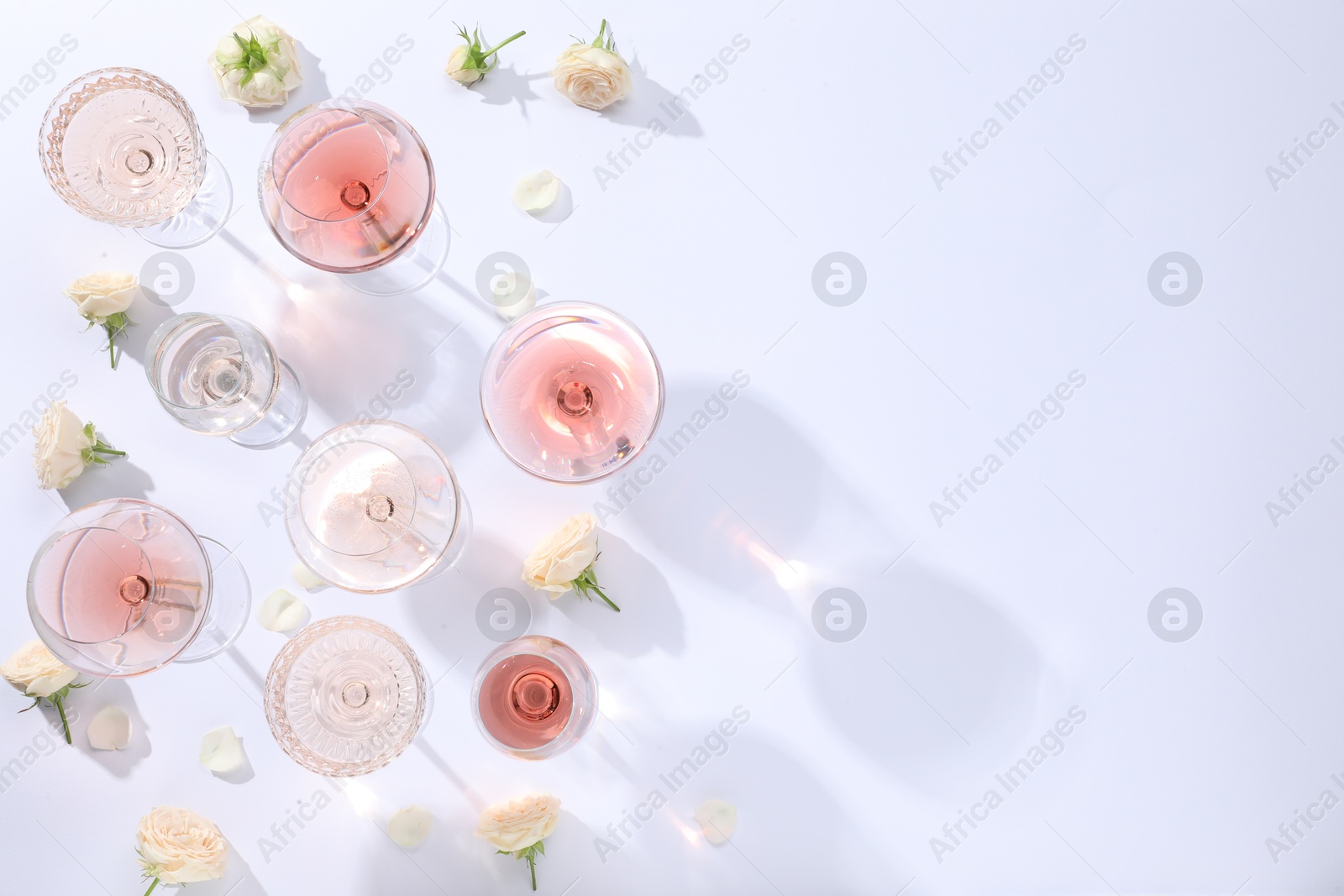 Photo of Delicious rose wine in glasses and flowers on white background, flat lay. Space for text