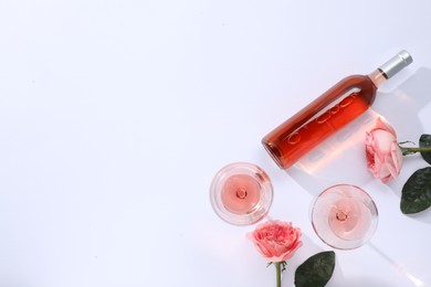 Delicious rose wine in glasses and bottle with flowers on white background, flat lay. Space for text