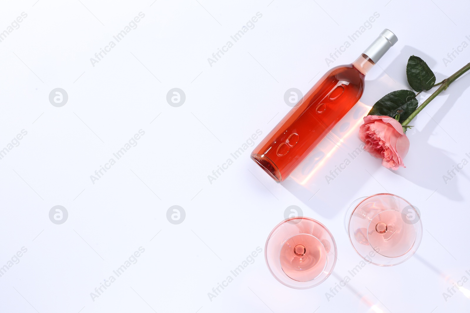 Photo of Delicious rose wine in glasses and bottle with flower on white background, flat lay. Space for text