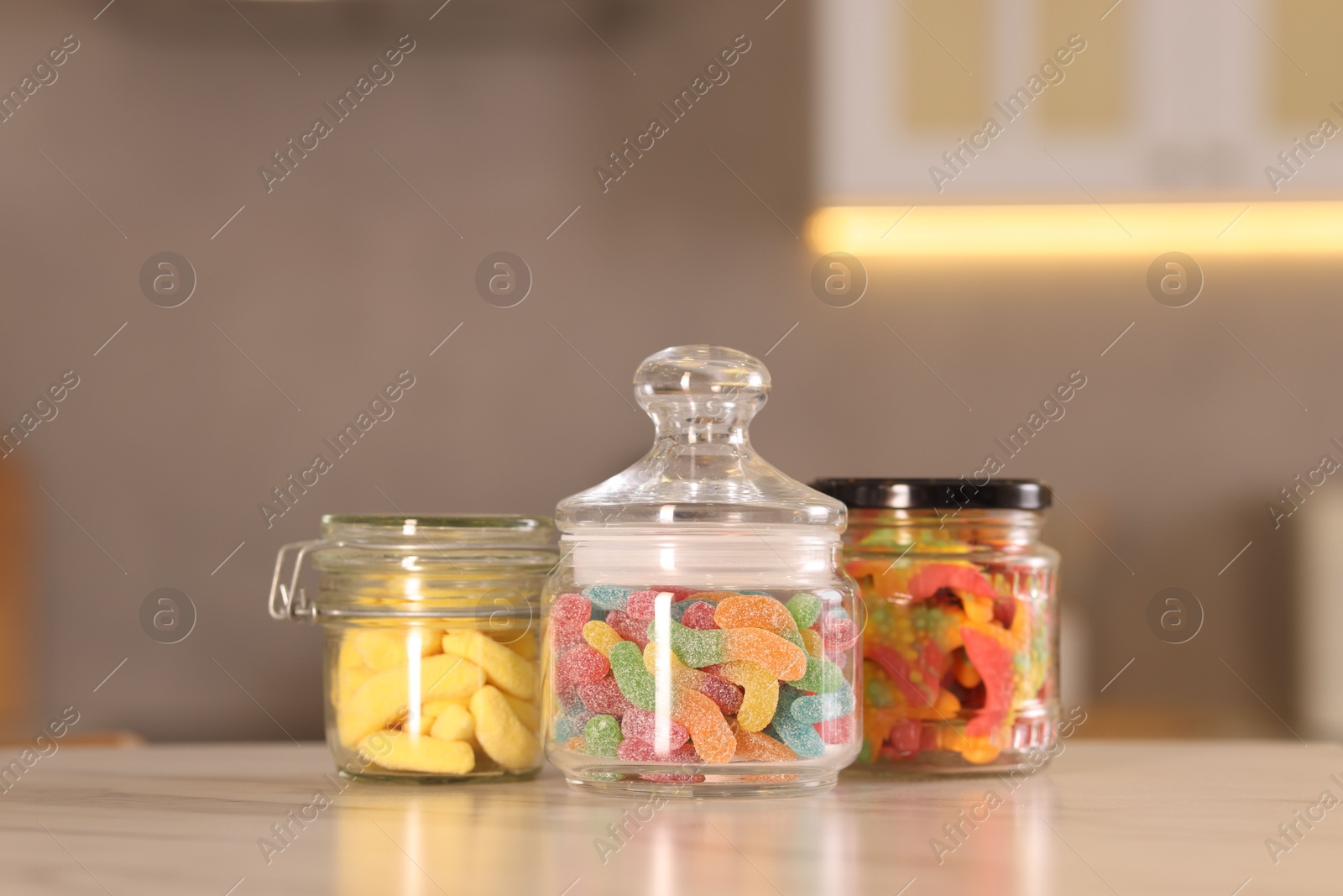 Photo of Tasty gummy candies in glass jars on white marble table