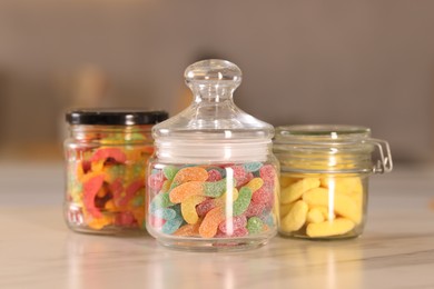 Photo of Tasty gummy candies in glass jars on white marble table, closeup