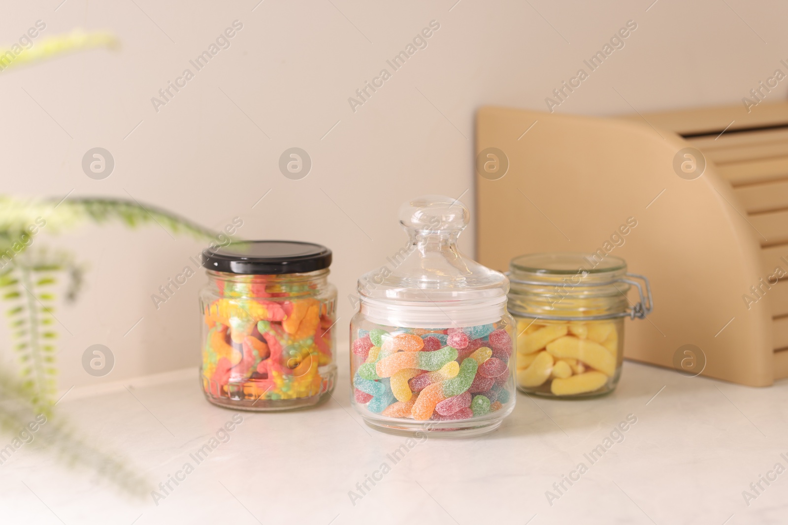 Photo of Tasty gummy candies in glass jars on white table