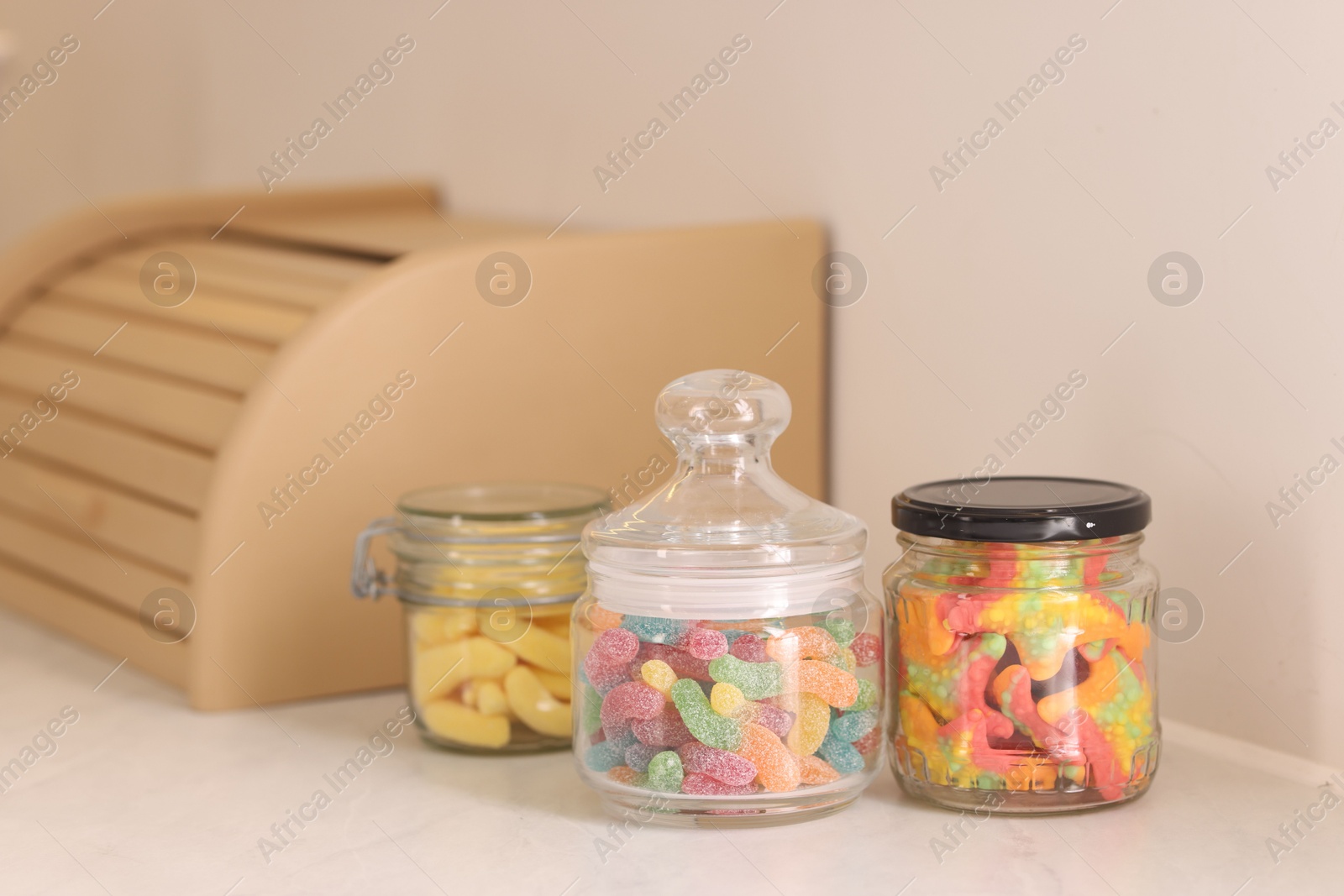 Photo of Tasty gummy candies in glass jars on white table