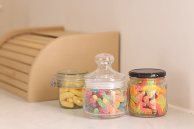 Photo of Tasty gummy candies in glass jars on white table