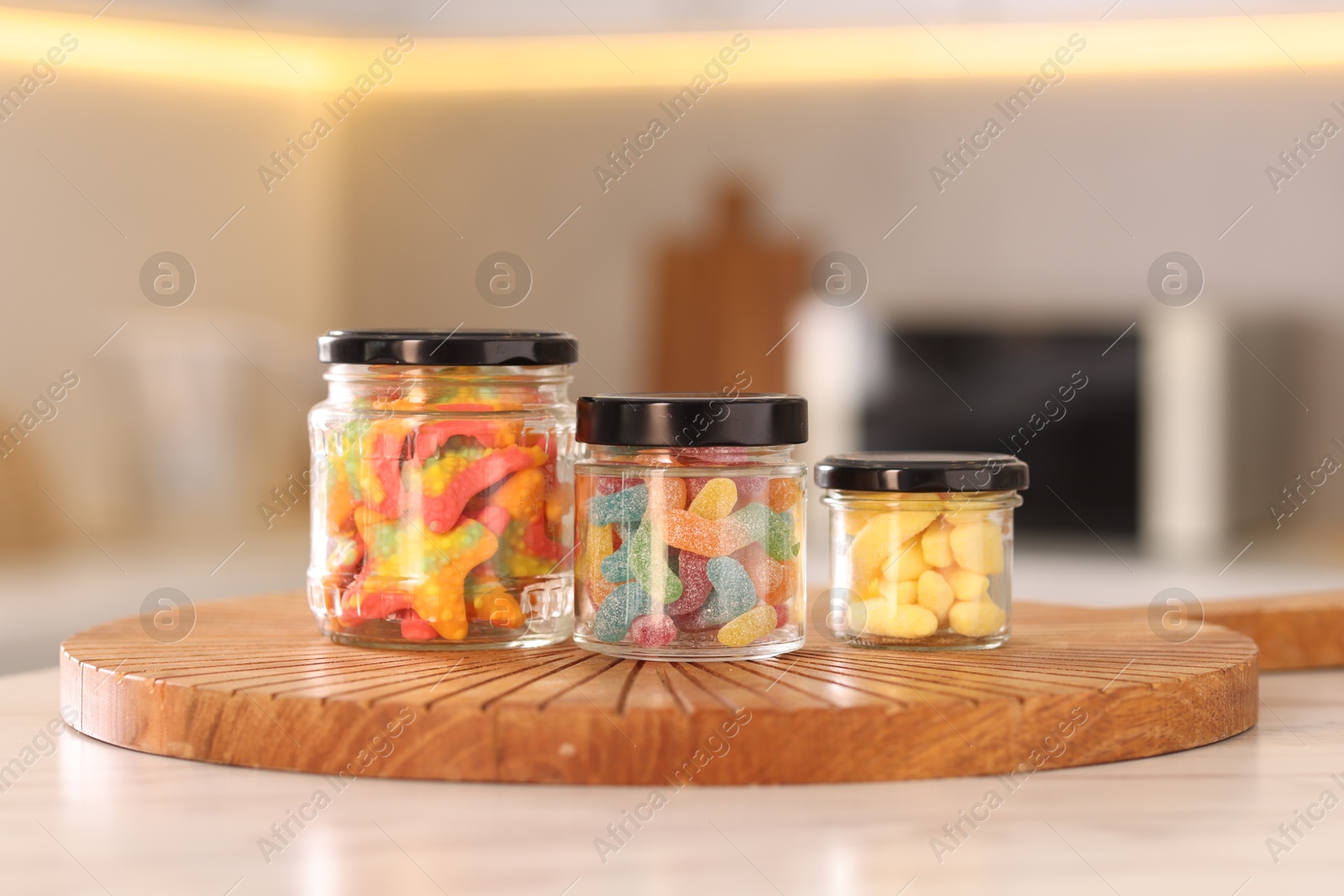 Photo of Tasty gummy candies in glass jars on white table