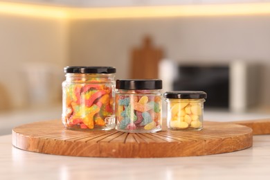 Photo of Tasty gummy candies in glass jars on white table