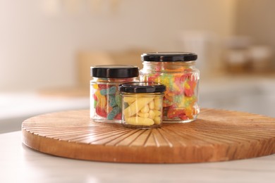 Photo of Tasty gummy candies in glass jars on white table