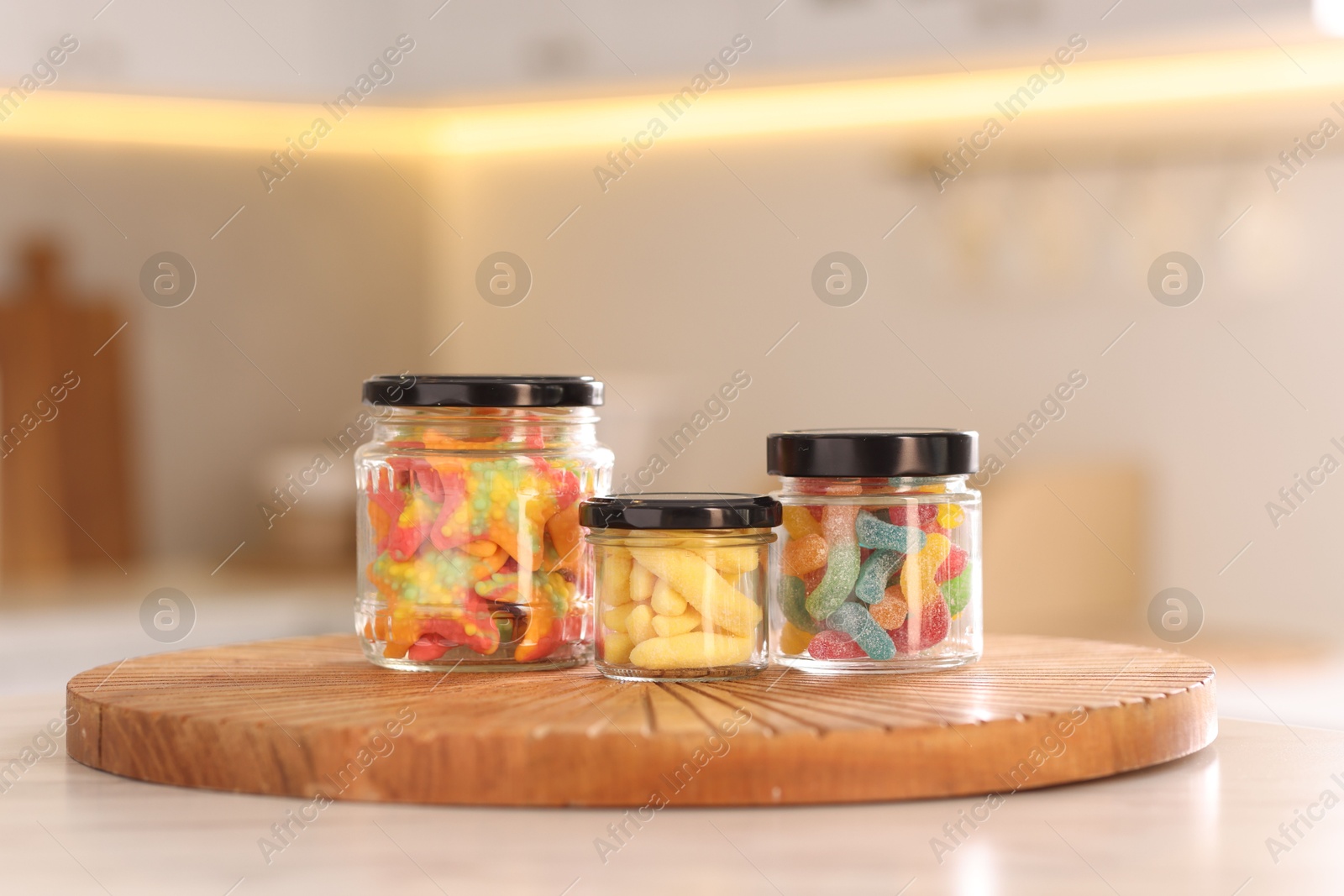 Photo of Tasty gummy candies in glass jars on white table