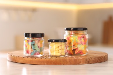 Photo of Tasty gummy candies in glass jars on white table