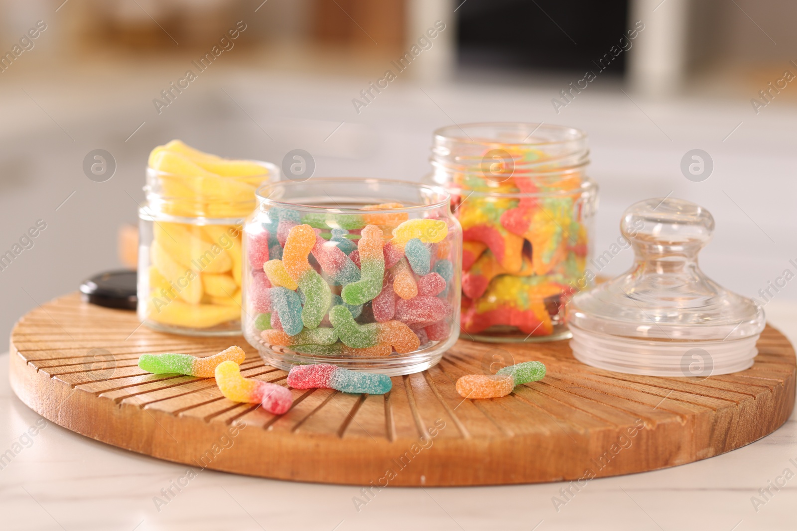 Photo of Tasty gummy candies in glass jars on white table