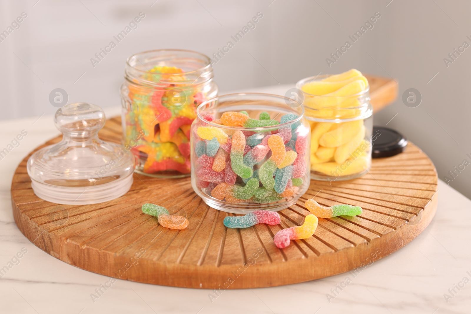 Photo of Tasty gummy candies in glass jars on white table