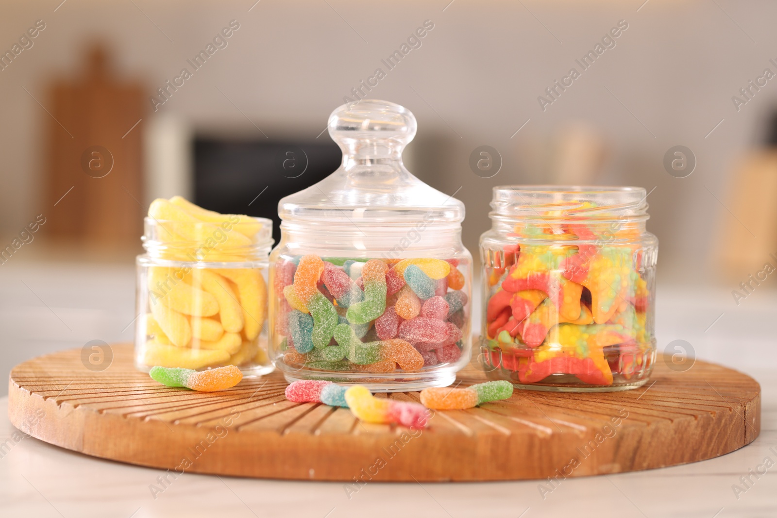 Photo of Tasty gummy candies in glass jars on white table