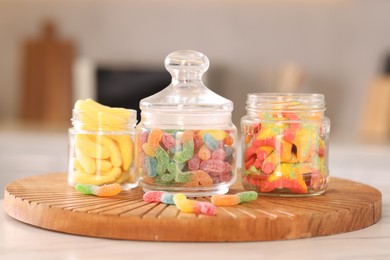 Photo of Tasty gummy candies in glass jars on white table