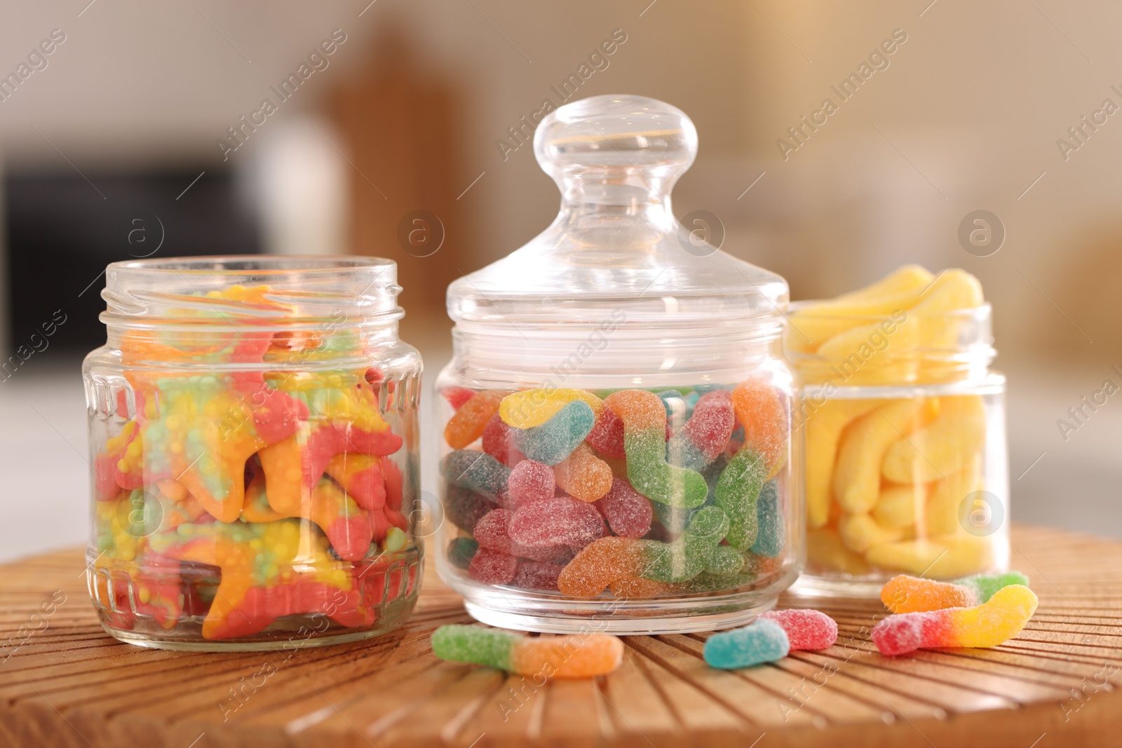 Photo of Tasty gummy candies in glass jars on wooden board, closeup